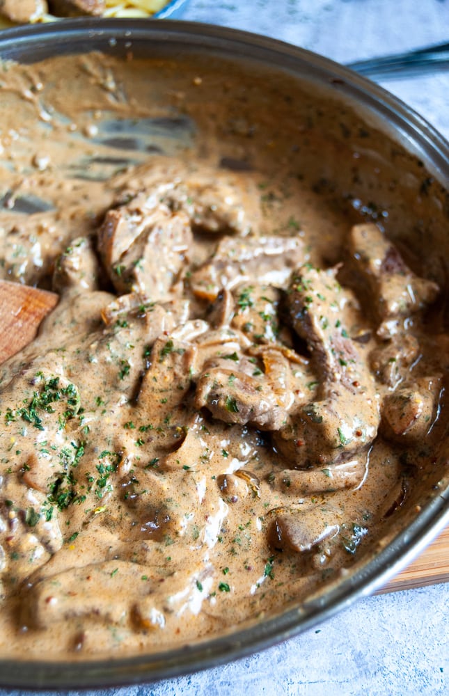 a close up picture of a pan of slices of rump steak, sliced onions and mushrooms in a sour cream sauce.