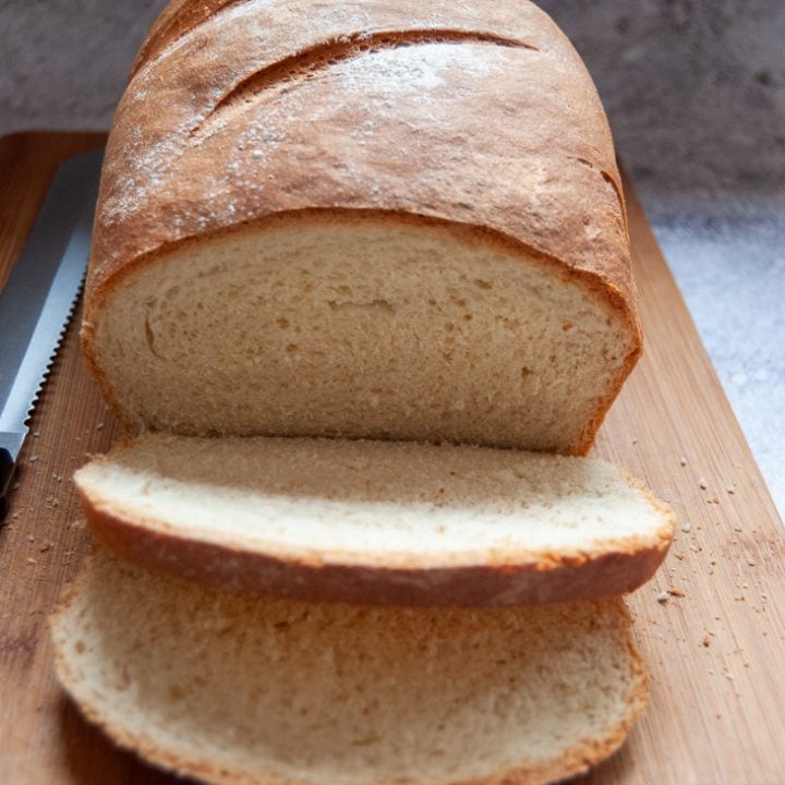 A homemade loaf of bread partially cut into slices on a wooden chopping board.