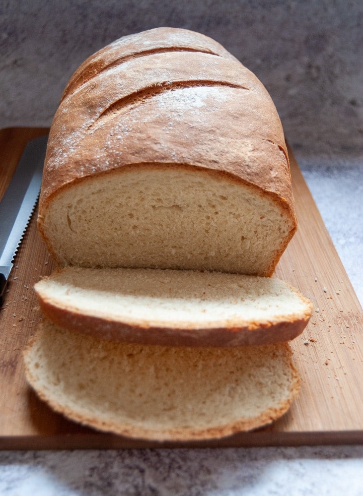 A homemade loaf of bread partially cut into slices on a wooden chopping board.