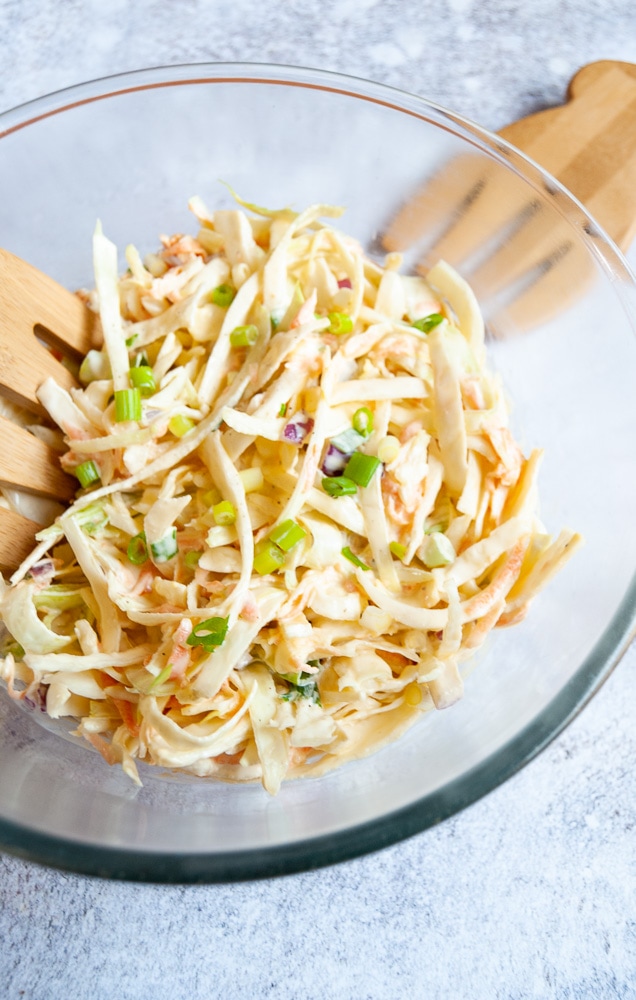 A bowl of coleslaw with wooden serving hands