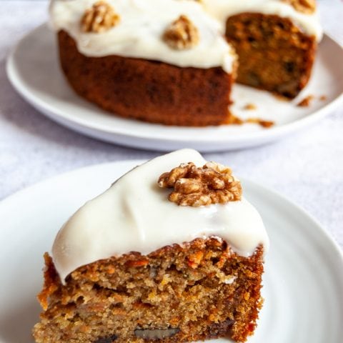 A slice of carrot cake topped with cream cheese icing and a walnut on a white plate.