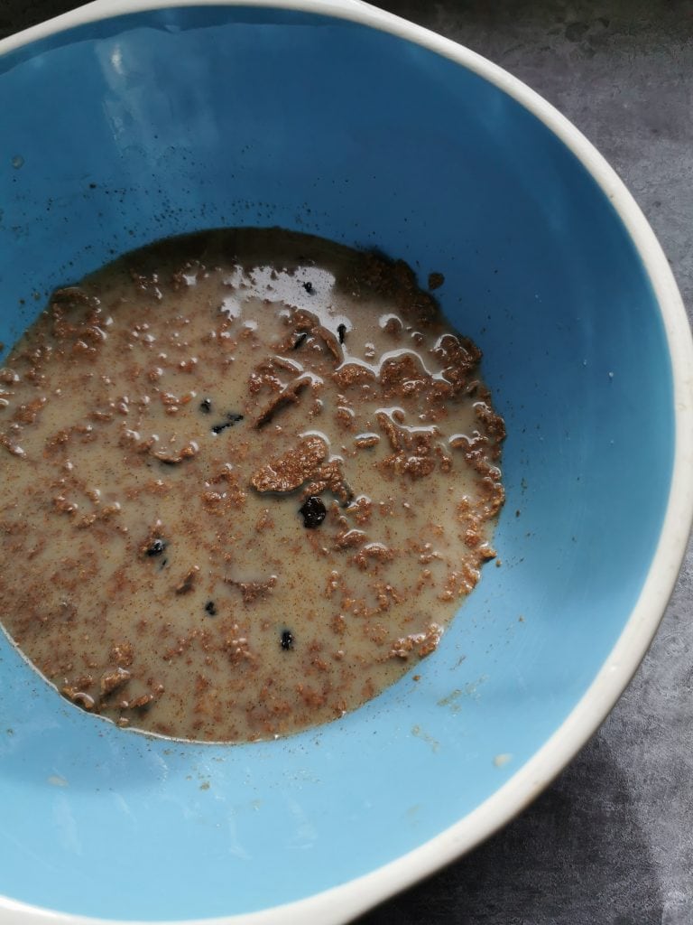 A blue and white bowl of bran flakes, milk and dried fruit