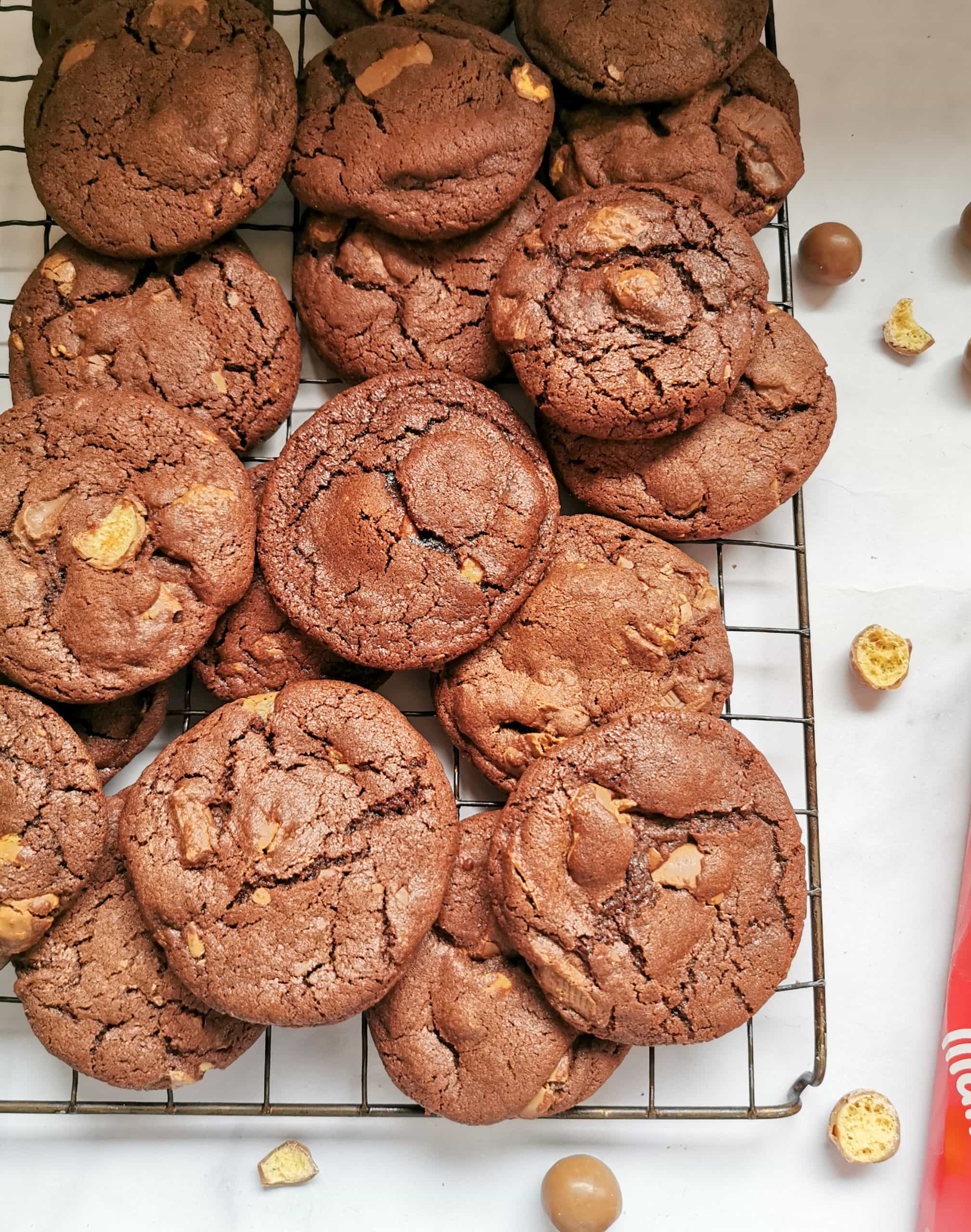 A pile of chocolate cookies with chocolate chips and Maltesers on a wire rack.