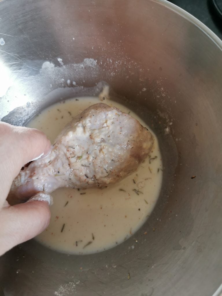 A chicken drumstick being coated in a spiced buttermilk mixture