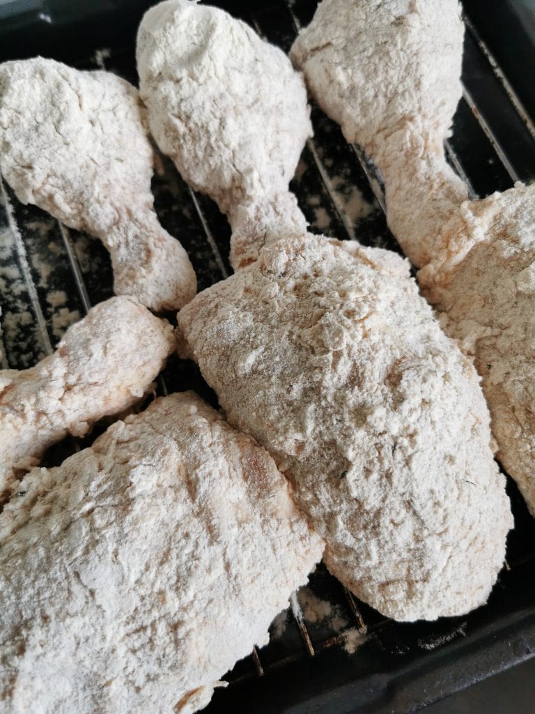 Chicken thighs and drumstick pieces coated in a spiced flour mixture on a wire rack