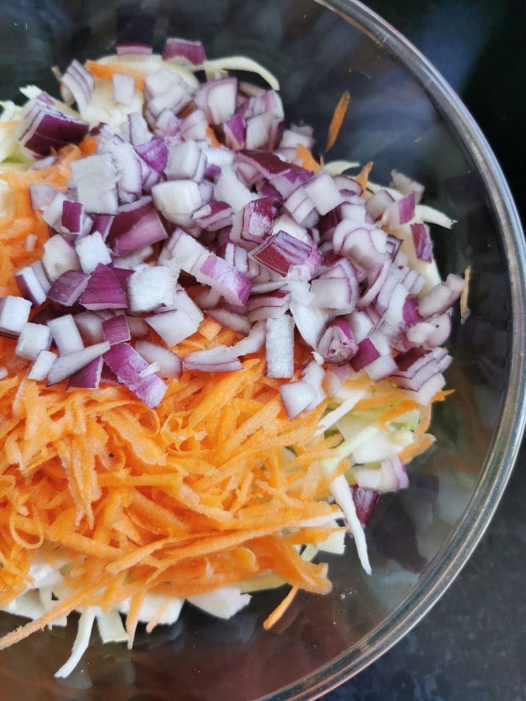 shredded white cabbage, carrots and diced red onion in a silver bowl