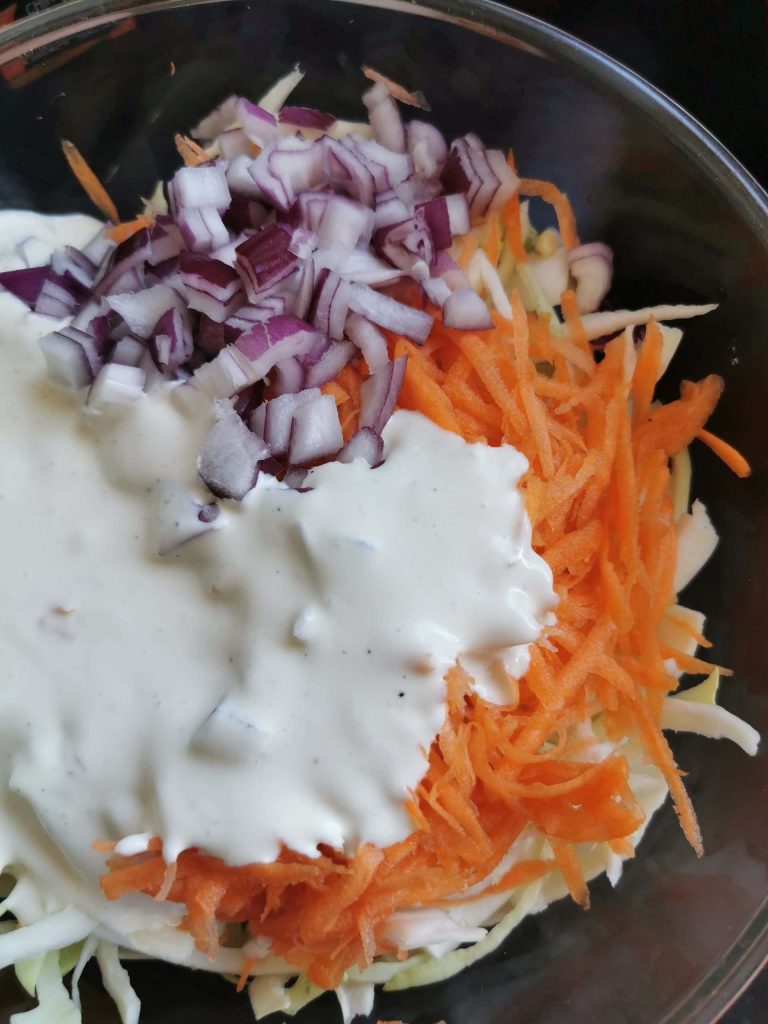 shredded cabbage, carrots and diced onion in a bowl with slaw dressing