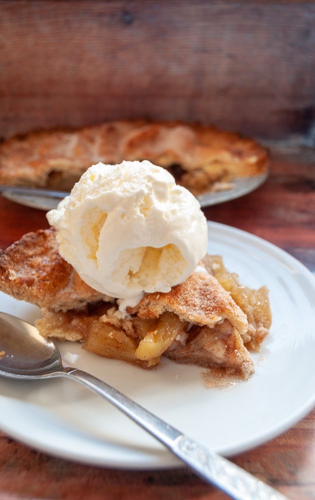 A slice of homemade apple pie with a scoop of vanilla ice cream on top 