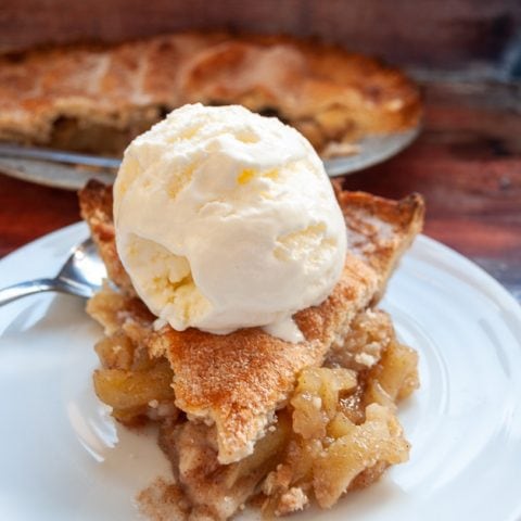 A slice of apple pie topped with a scoop of vanilla ice cream