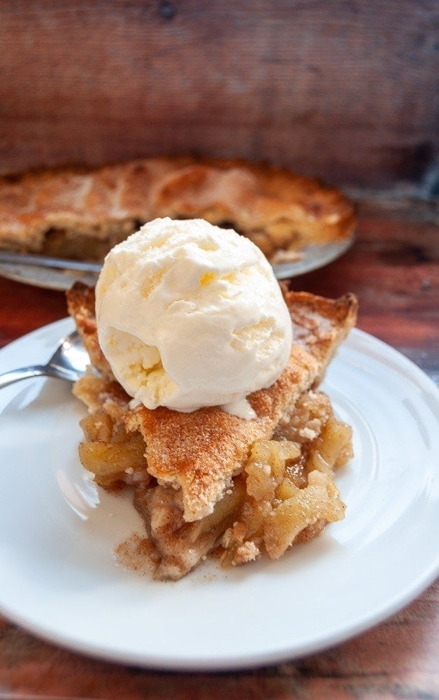 A slice of apple pie topped with a scoop of vanilla ice cream