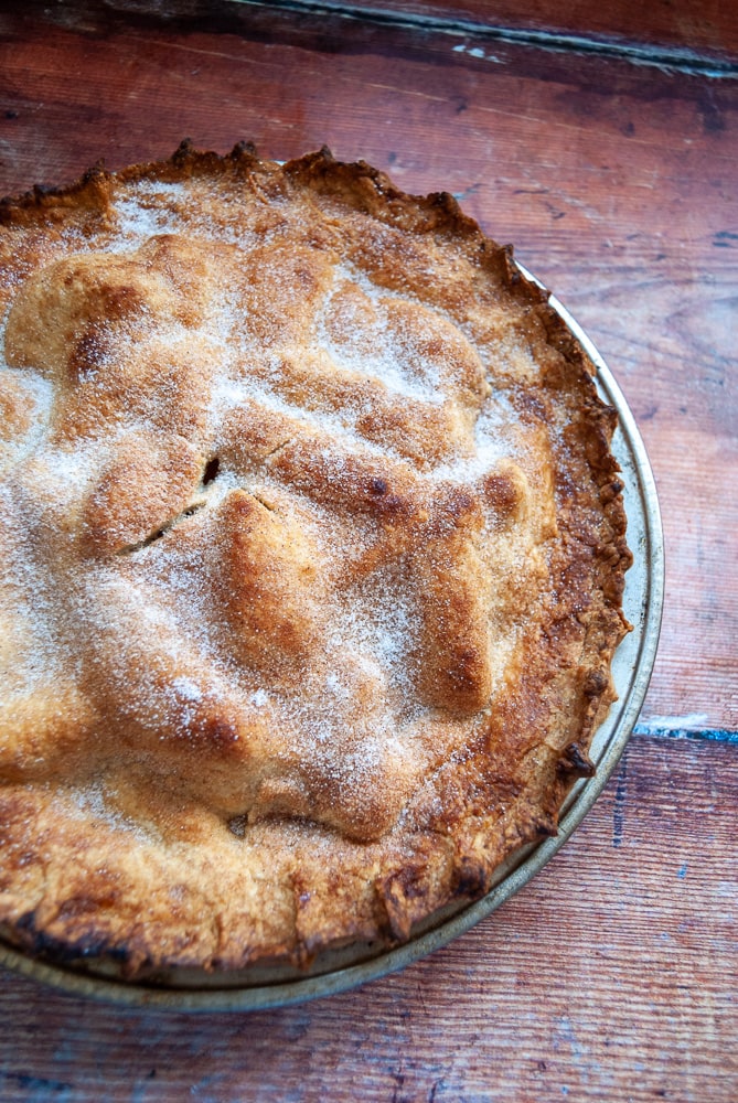 an apple pie in a metal pie dish on a wooden background