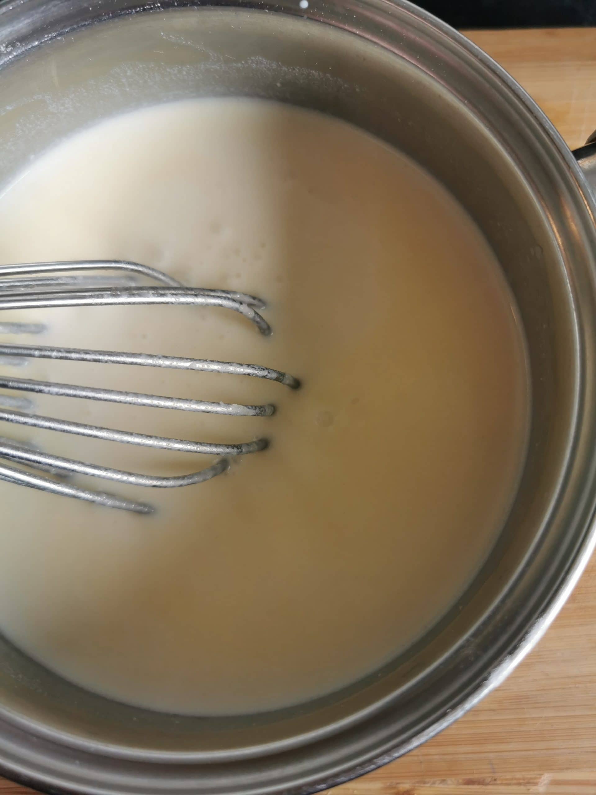 A pan of white sauce and a silver whisk.