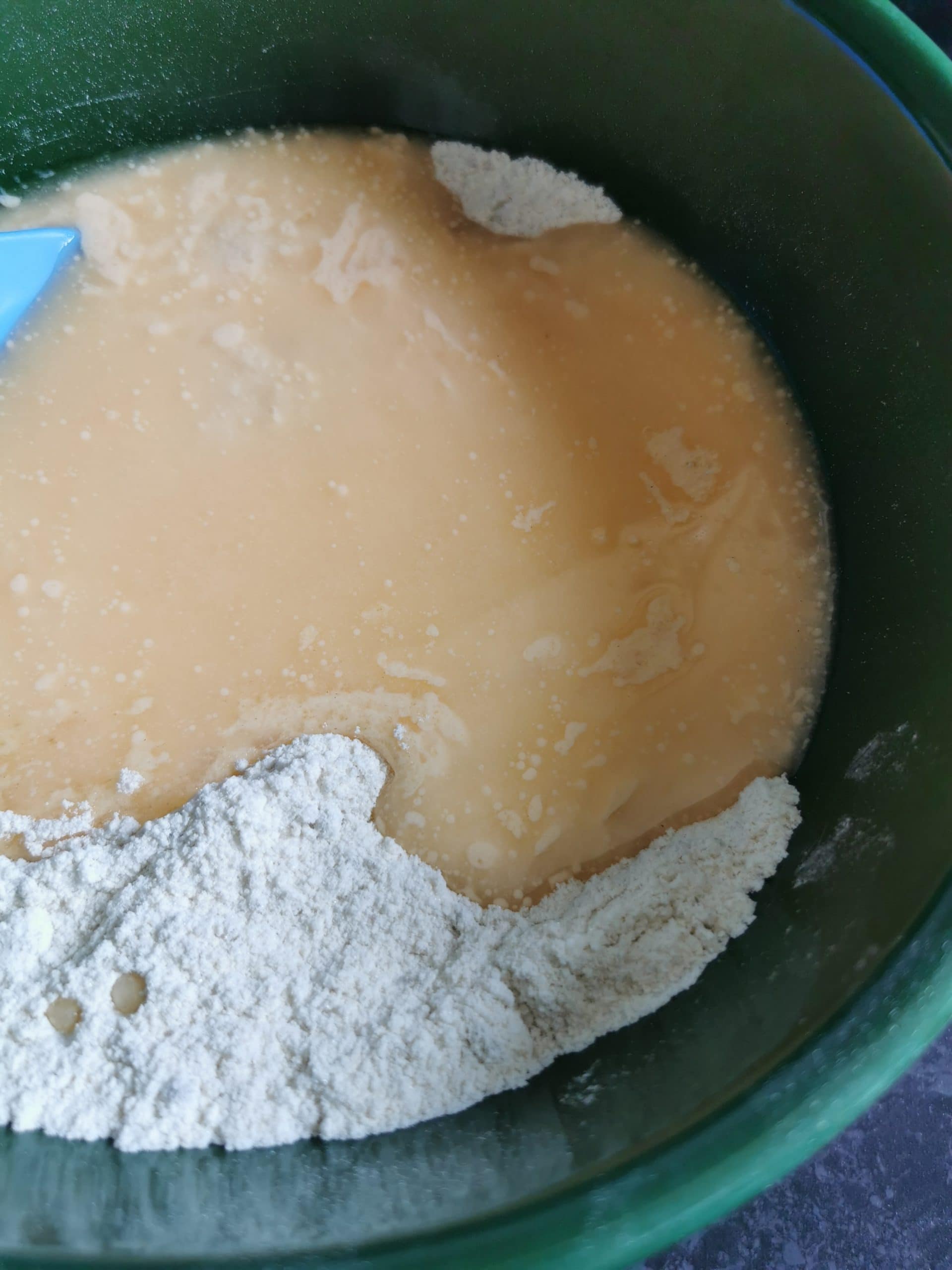A green bowl of eggs and sour cream being mixed into flour.