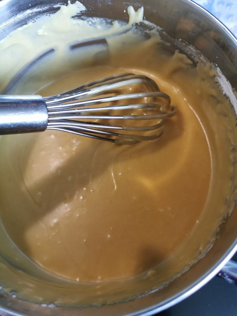 A mixture of golden syrup, butter, icing sugar and ginger in a saucepan with a whisk 