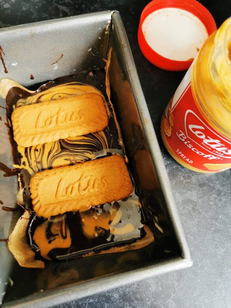 a mini loaf pan with brownie batter swirled with biscoff spread and topped with biscoff cookies