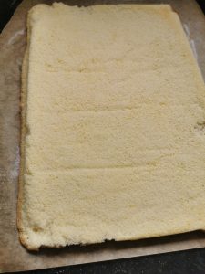 A rectangular whisked sponge on a piece of baking paper