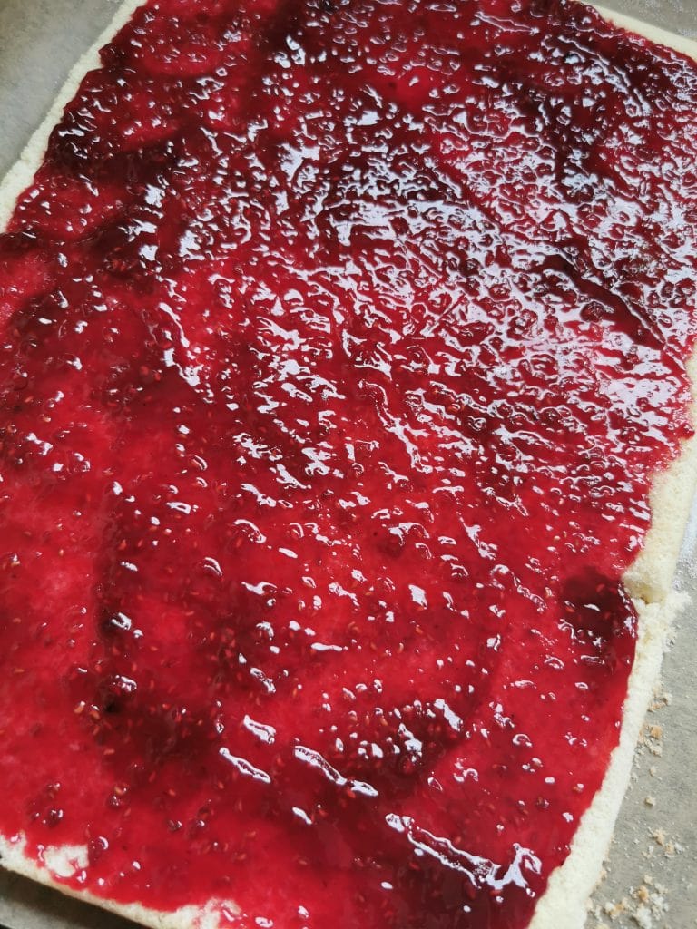 A rectangular sponge cake spread with raspberry jam