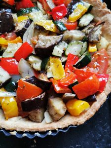 A pastry case lined with diced aubergine, red pepper, yellow peppers, and onion.
