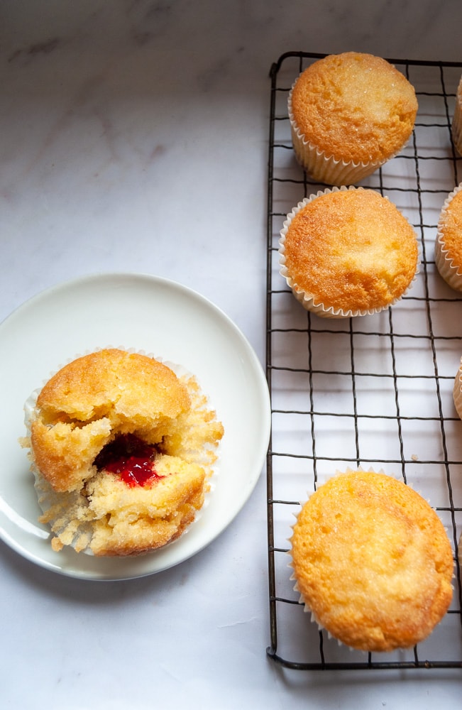 A lemon drizzle cupcake with a jam filling on a white plate.