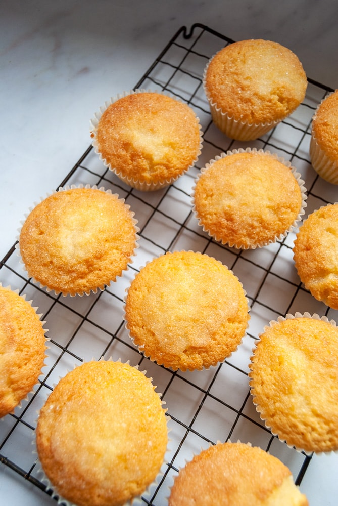 A batch of lemon drizzle cupcakes with a sugar topping on a black wire rack