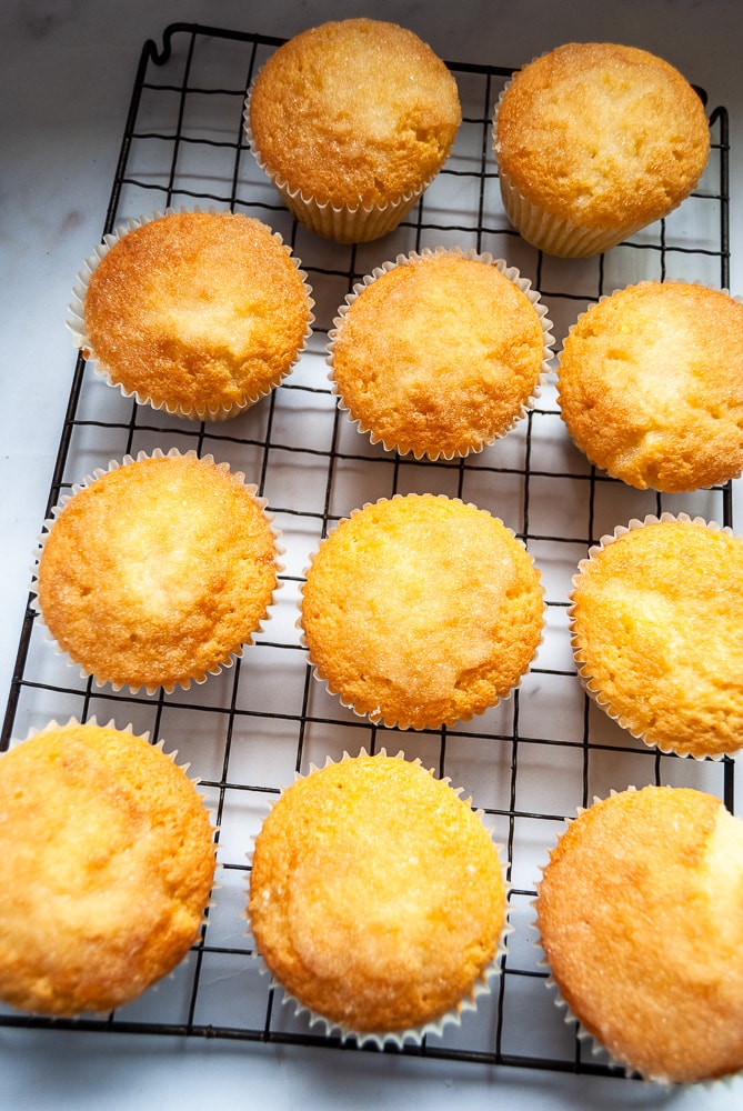 A batch of lemon drizzle cupcakes on a black wire rack