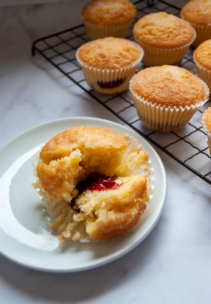 a lemon cupcake cut in half to reveal a raspberry jam filling on a white plate