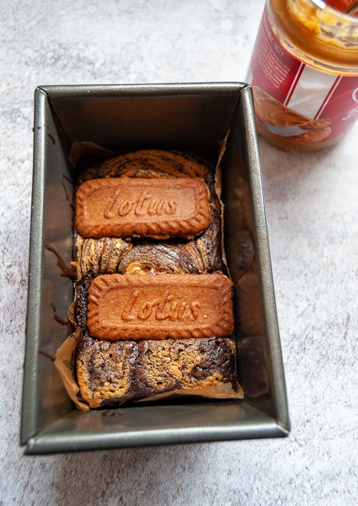 A small loaf pan with a chocolate brownie topped with Biscoff spread and a Biscoff cookie