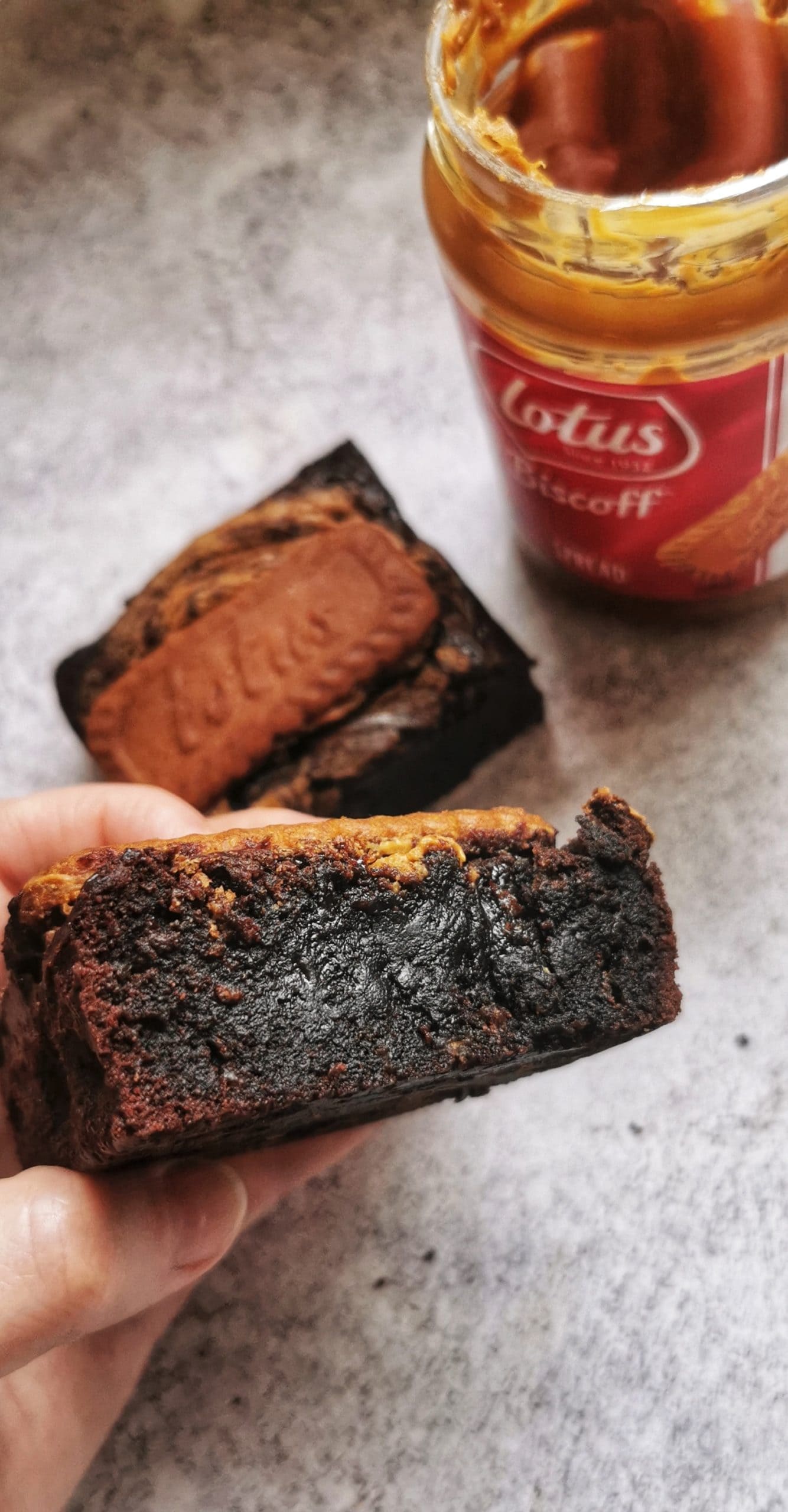 a hand holding a fudgy chocolate brownie with biscoff spread