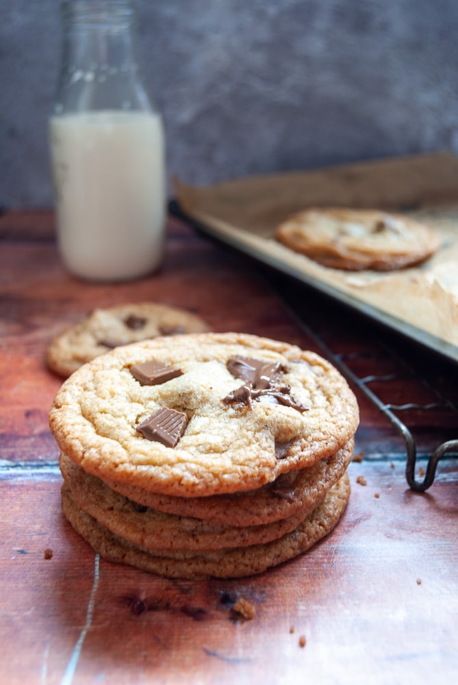 A stack of cookies studded with chocolate chunks on a wooden board