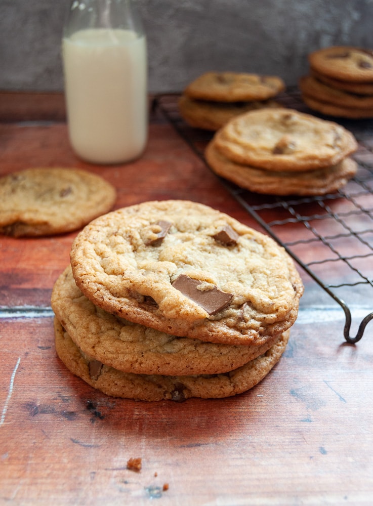 A stack of 3 chocolate chip cookies, a bottle of milk and more cookies on a wire rack