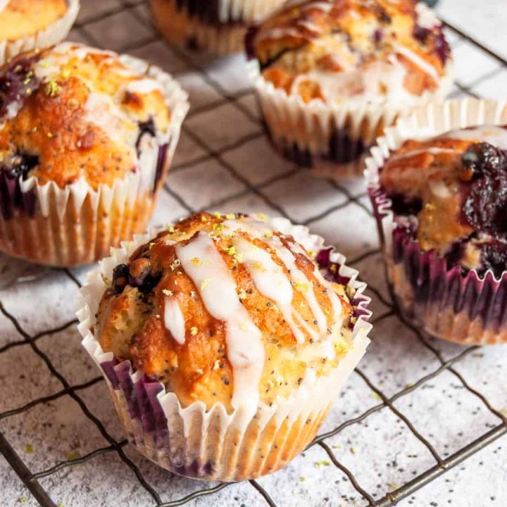 a batch of blueberry poppy seed muffins with a lime glaze on a silver wire rack.