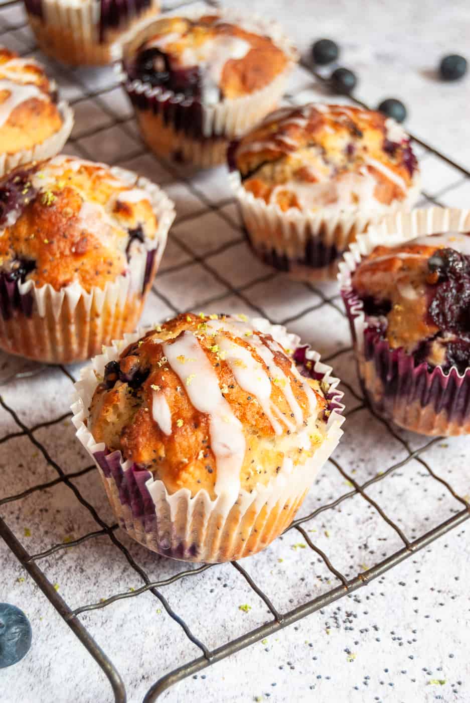 a batch of blueberry poppy seed muffins with a lime glaze on a silver wire rack.