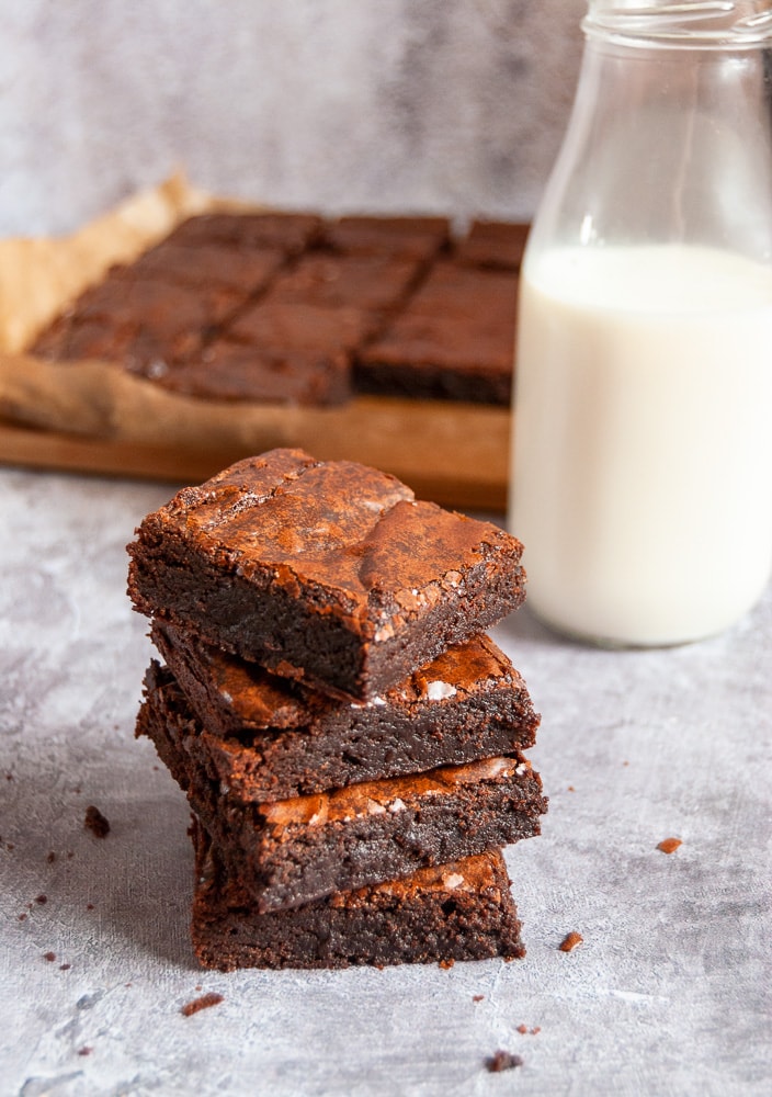 A stack of four brownies, a glass bottle of milk and more brownies on a wooden board