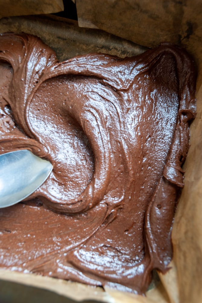 Brownie batter being spooned into a square tin