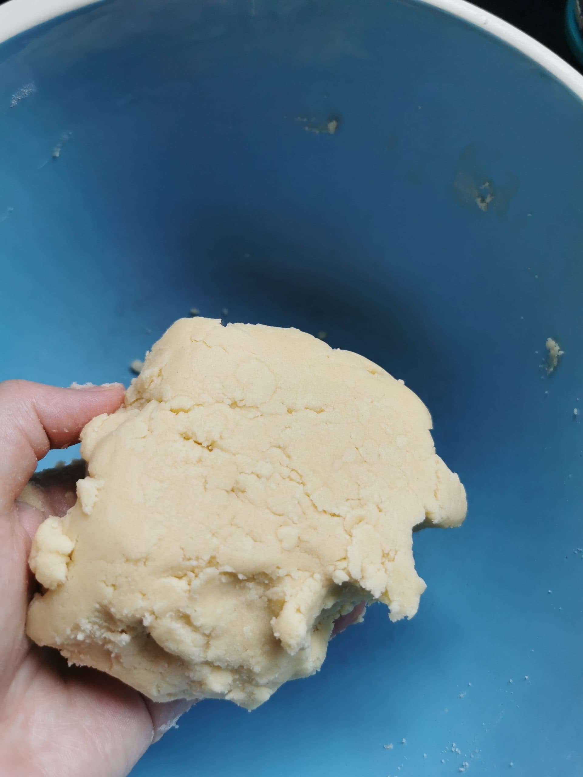 A hand holding a piece of shortbread dough in a blue bowl