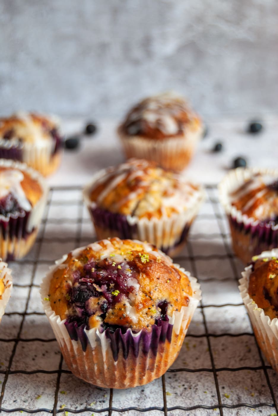 A close up photo of blueberry poppy seed muffins topped with a lime glaze on a black wire rack.