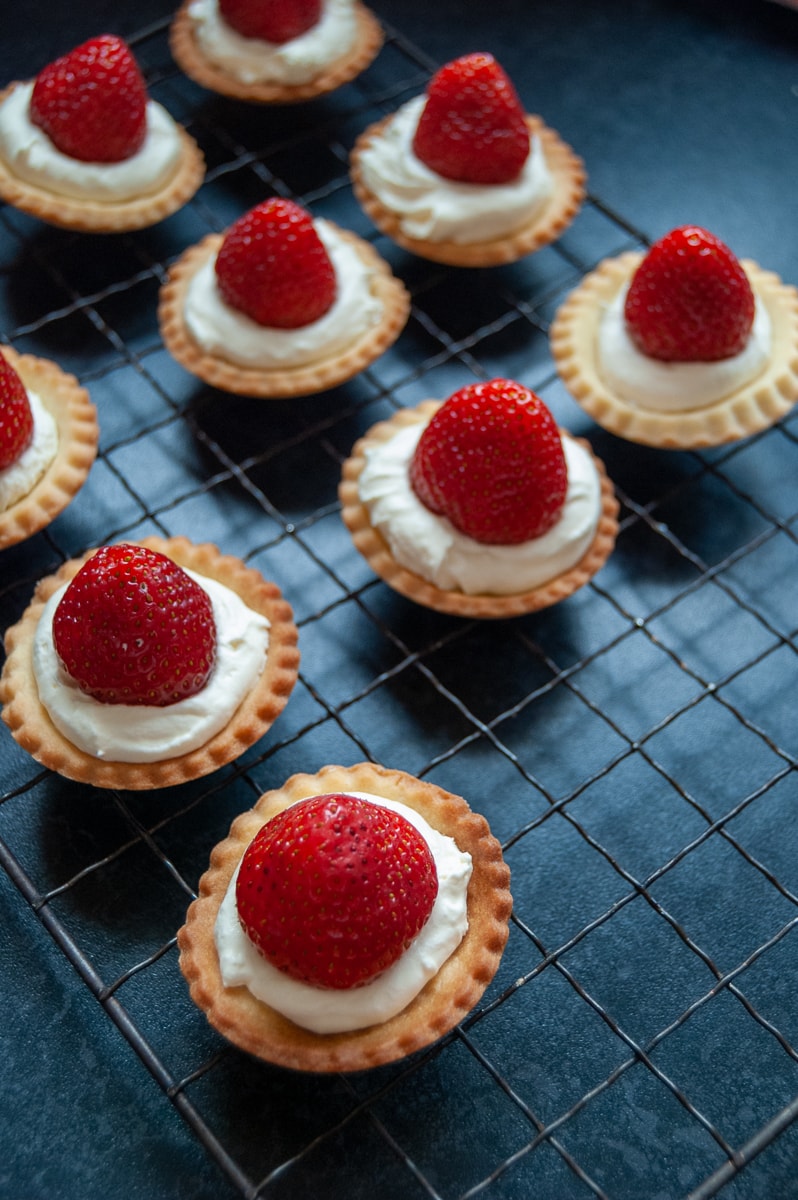 Freshly made strawberry tarts on a black wire rack