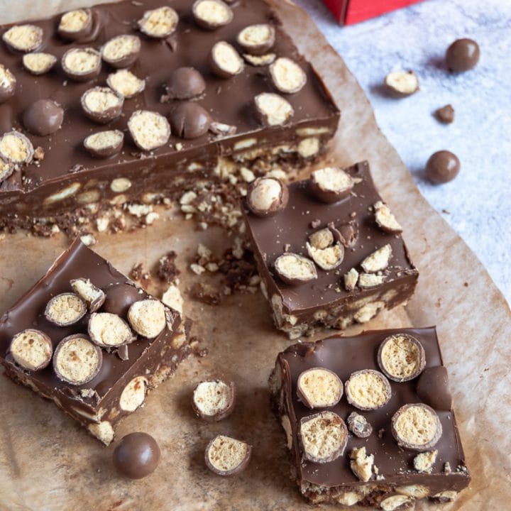 Square of Malteser traybake on a piece of baking paper and a box of Maltesers