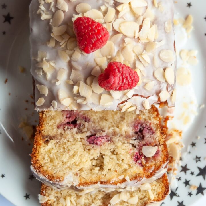 A raspberry cake covered in white icing, flaked almonds and fresh raspberries on a white and gold star plate