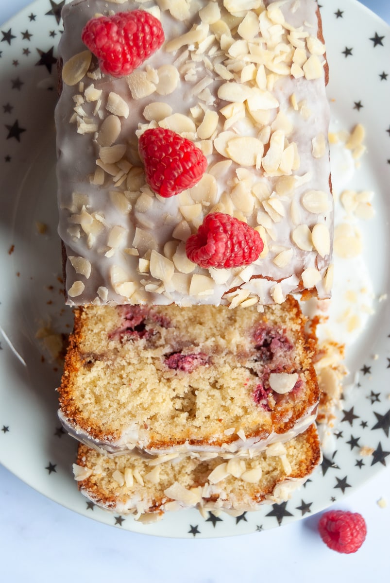 A raspberry cake covered in white icing, flaked almonds and fresh raspberries on a white and gold star plate