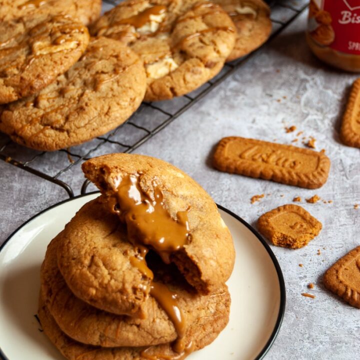 Three biscoff cookies on a white plate drizzled with warm biscoff spread, more cookies on a wire rack and Biscoff cookies and a jar of Biscoff spread