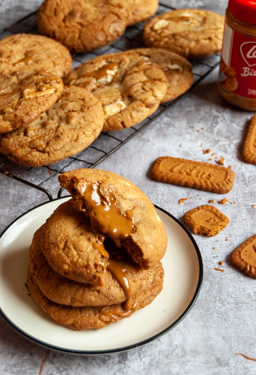 Three biscoff cookies on a white plate drizzled with warm biscoff spread, more cookies on a wire rack and Biscoff cookies and a jar of Biscoff spread