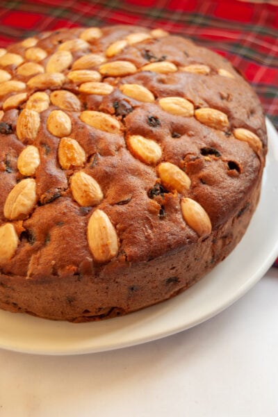 a close up photo of a Scottish Dundee fruit cake studded with whole almonds on a white plate