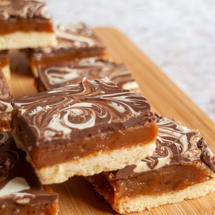 A stack of caramel shortbread topped with milk and white chocolate on a wooden board