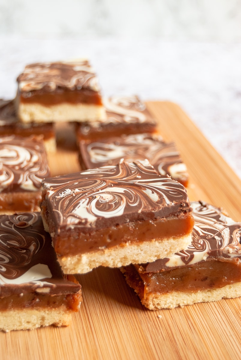 a stack of caramel shortbread topped with milk and white chocolate on a wooden board