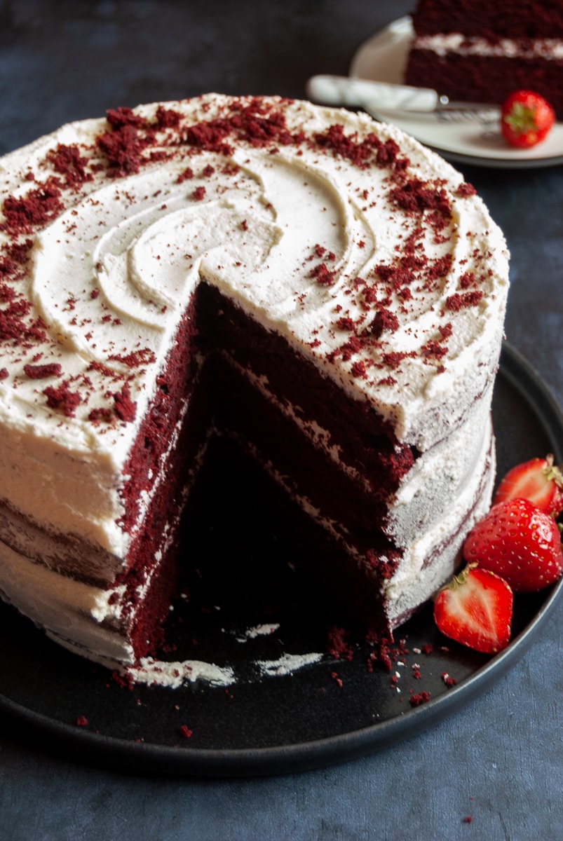 a red velvet cake with a slice cut out of it to reveal the inside on a black plate with fresh strawberries