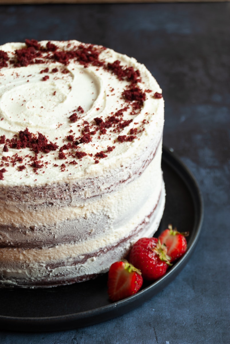  A red velvet cake covered in white chocolate buttercream on a black plate with fresh strawberries