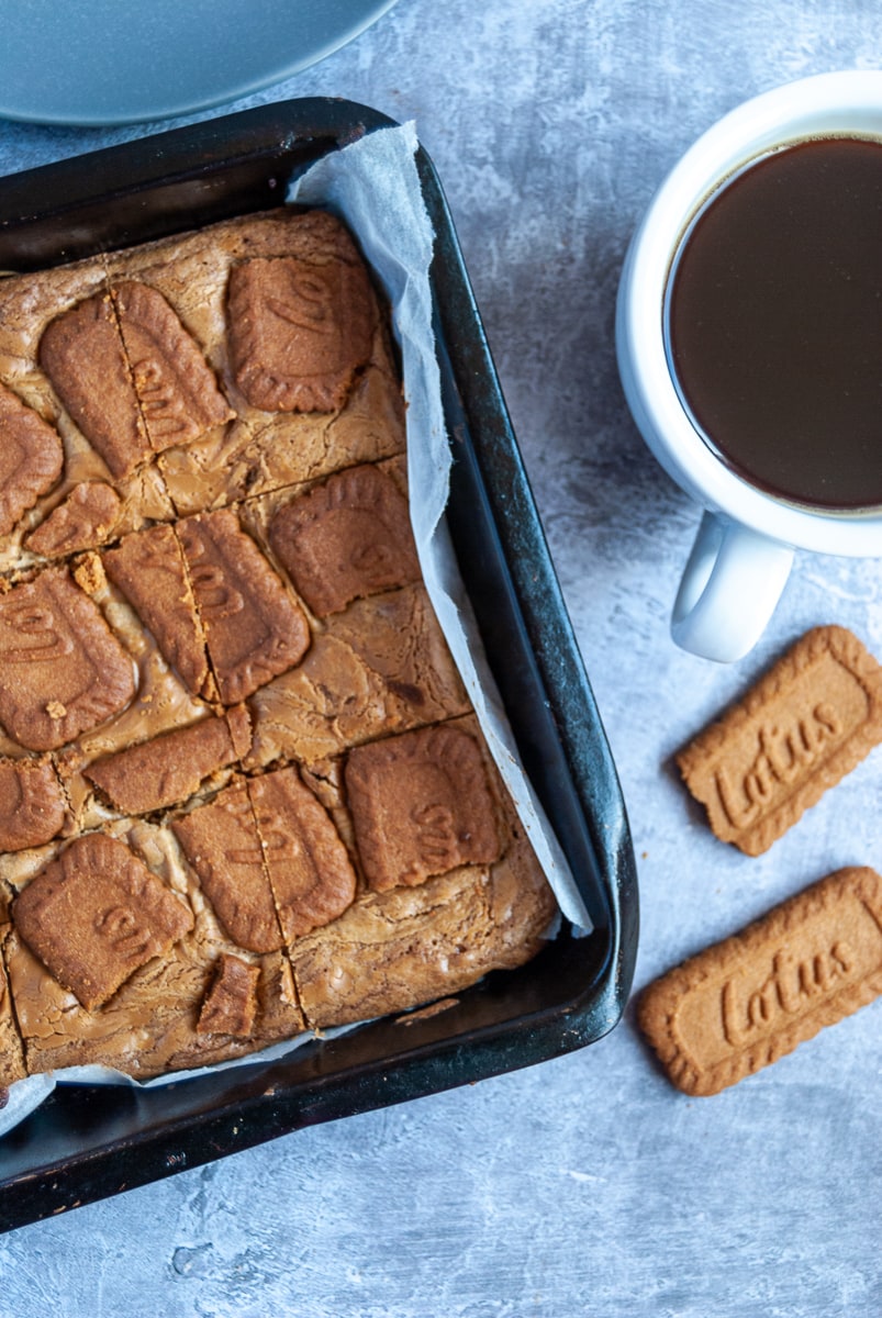 A tin of Biscoff blondies, a white cup of black coffee and two Lotus Biscoff cookies