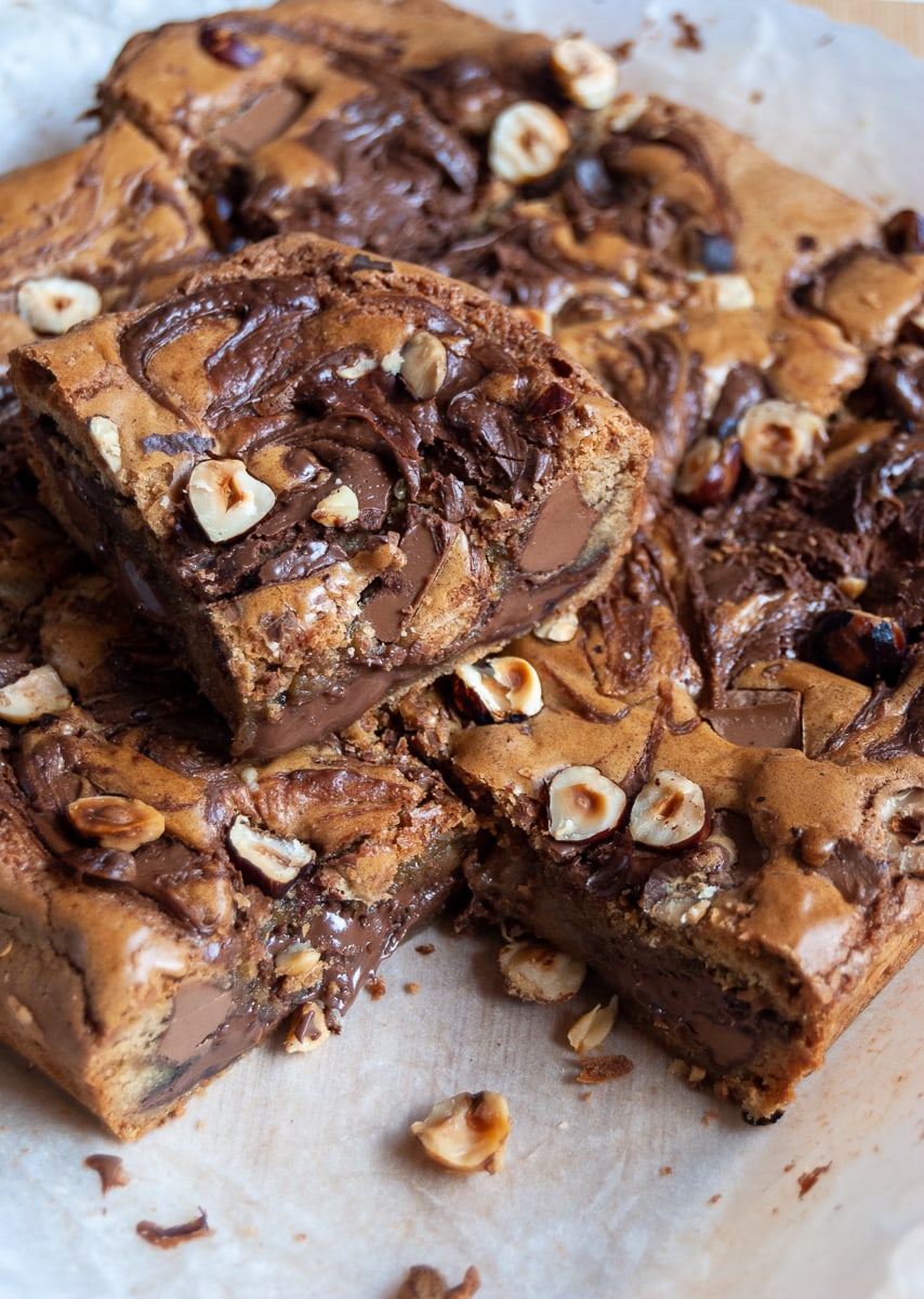 A batch of Nutella blondie bars scattered with hazelnuts on a piece of baking parchment.
