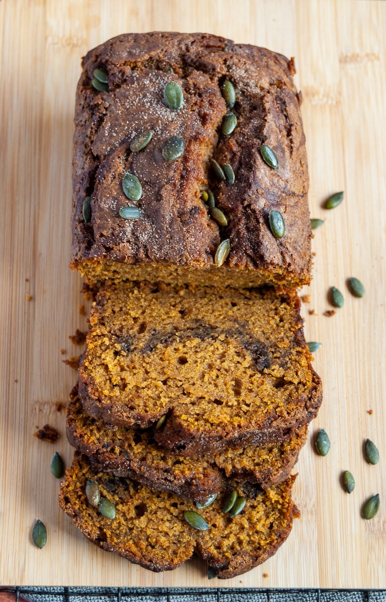 a partially sliced pumpkin spice loaf cake sprinkled with pumpkin seeds on a wooden board